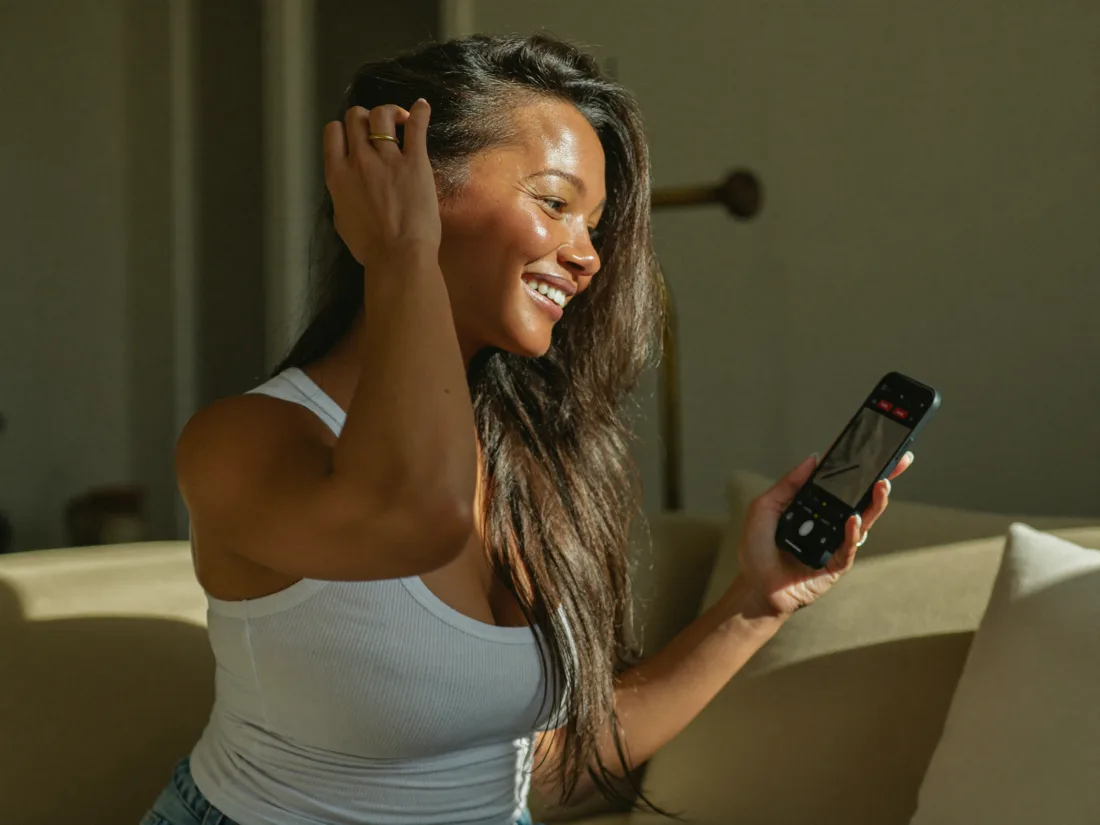 Mulher de cabelo saudável sorrindo enquanto assiste a uma aula no celular